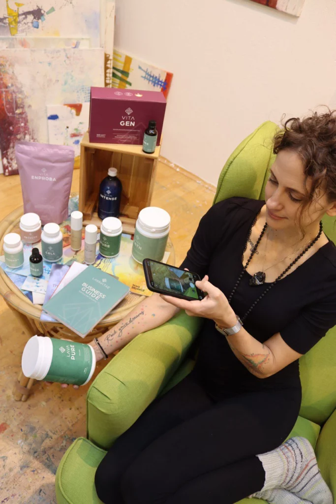 Stefanie Jahn von oben fotografiert wie sie in einem grünen Stuhl sitzend mit ihrem Handy ein Foto vom Produkt "Lava Pure" macht, dahinter weitere Produkte der Firma LAVAVITAE platziert.
